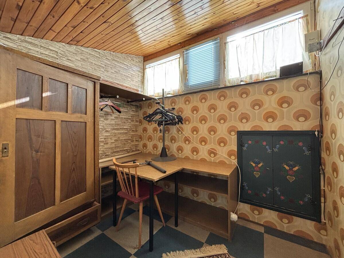 Kleiner Raum mit gemusterter Tapete, Holzdecke und Schreibtisch, bietet vielseitige Nutzungsmöglichkeiten.