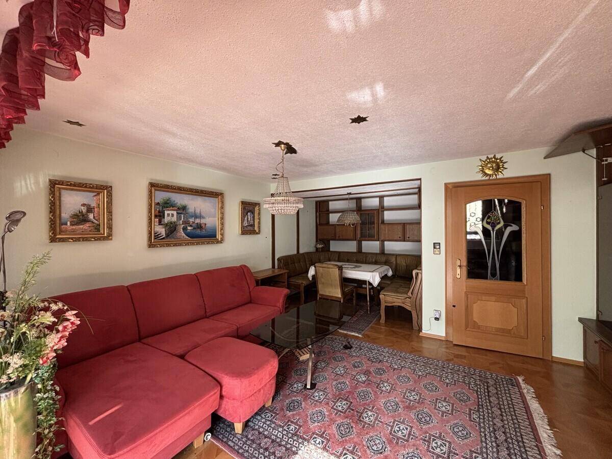 Wohn- und Essbereich mit rotem Sofa, traditionellen Holzmöbeln und dekorativen Bildern an der Wand.