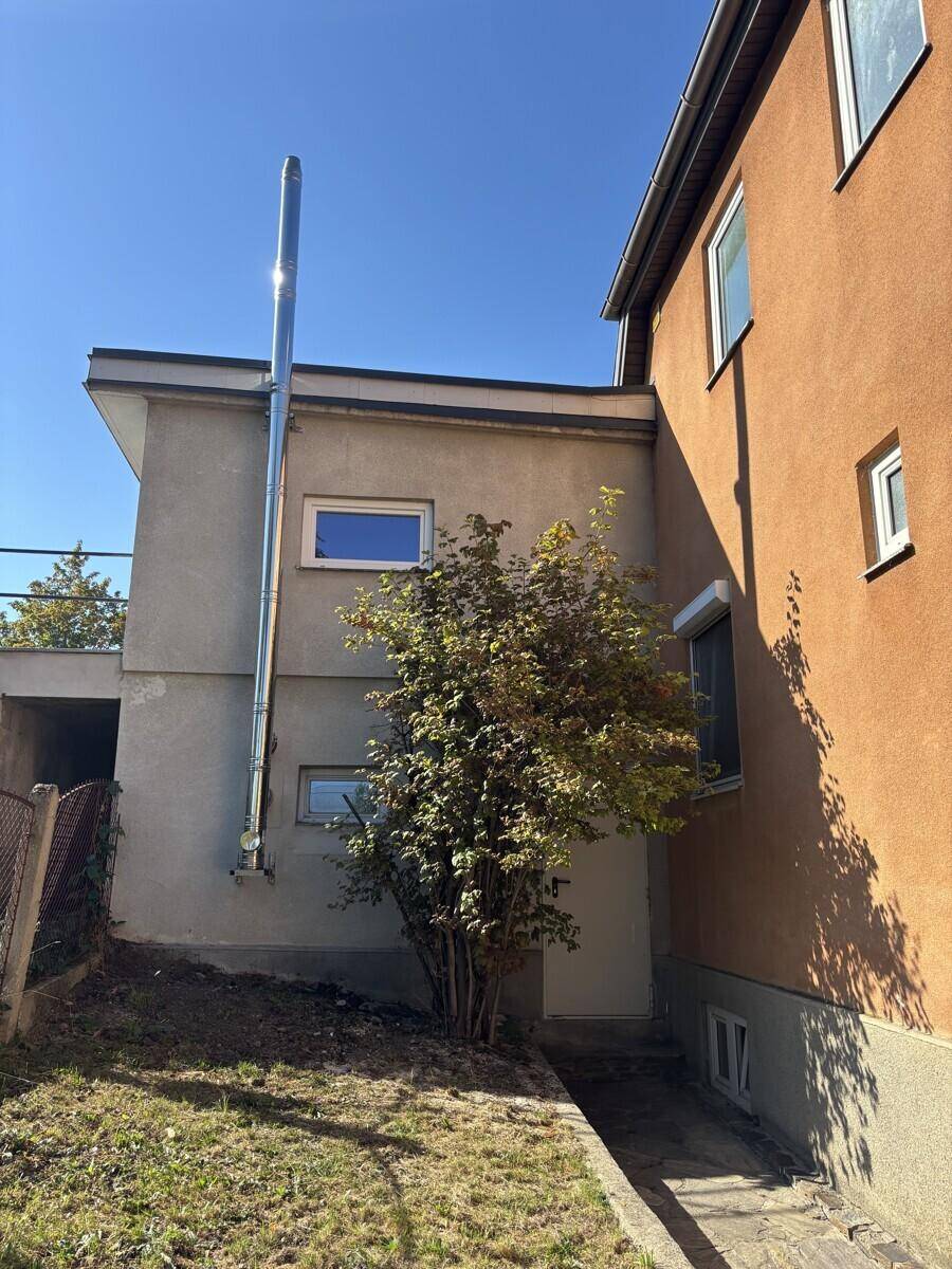 Seitenansicht eines Hauses mit Anbau und einem schmalen Gartenstreifen im Vordergrund.