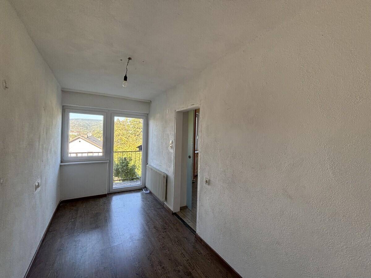 Helles Zimmer mit Laminatboden, weiß gestrichenen Wänden und Zugang zu einem Balkon.