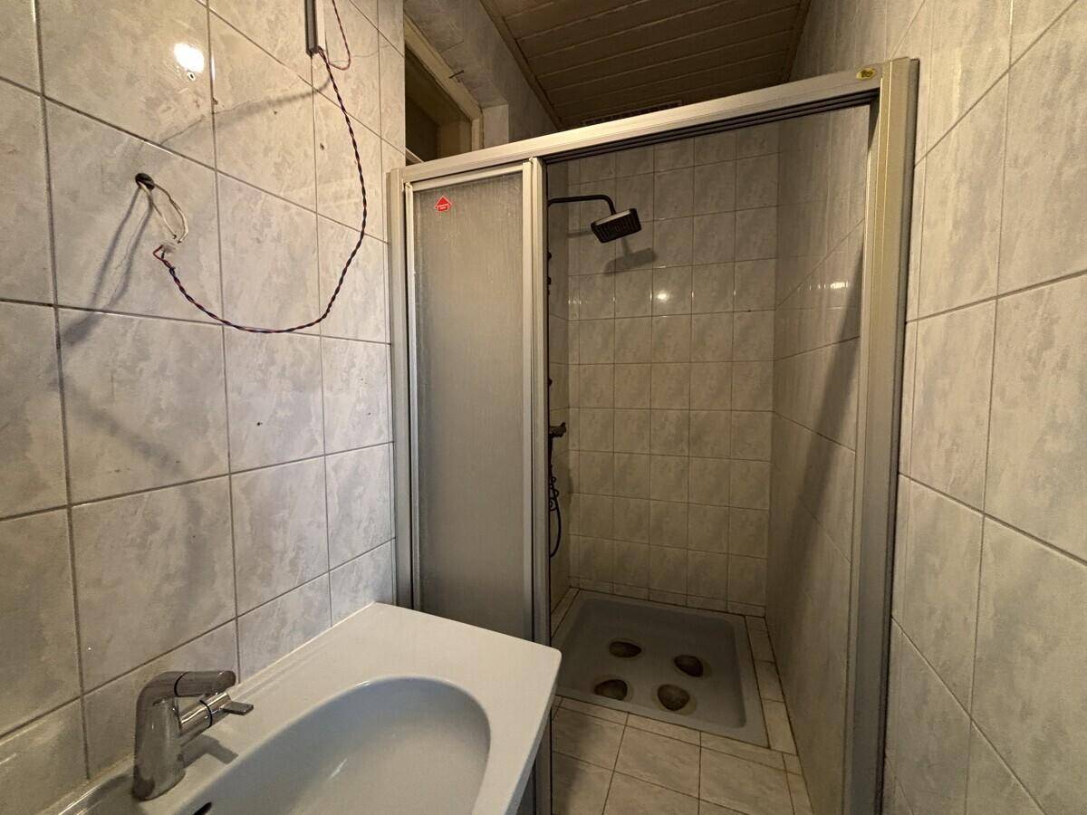 Badezimmer mit gefliesten Wänden, Duschkabine und einem Waschbecken.