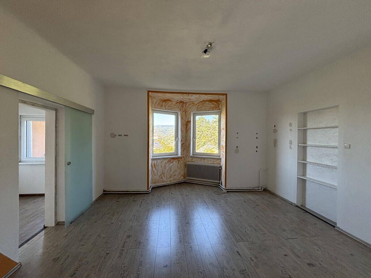 Helles Zimmer mit Laminatboden, Erkerfenster und integrierten Wandregalen.