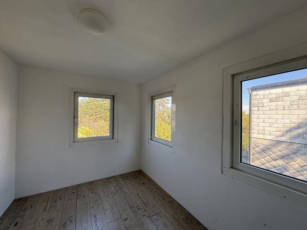 Kleines, helles Zimmer mit Laminatboden und mehreren Fenstern mit Ausblick.