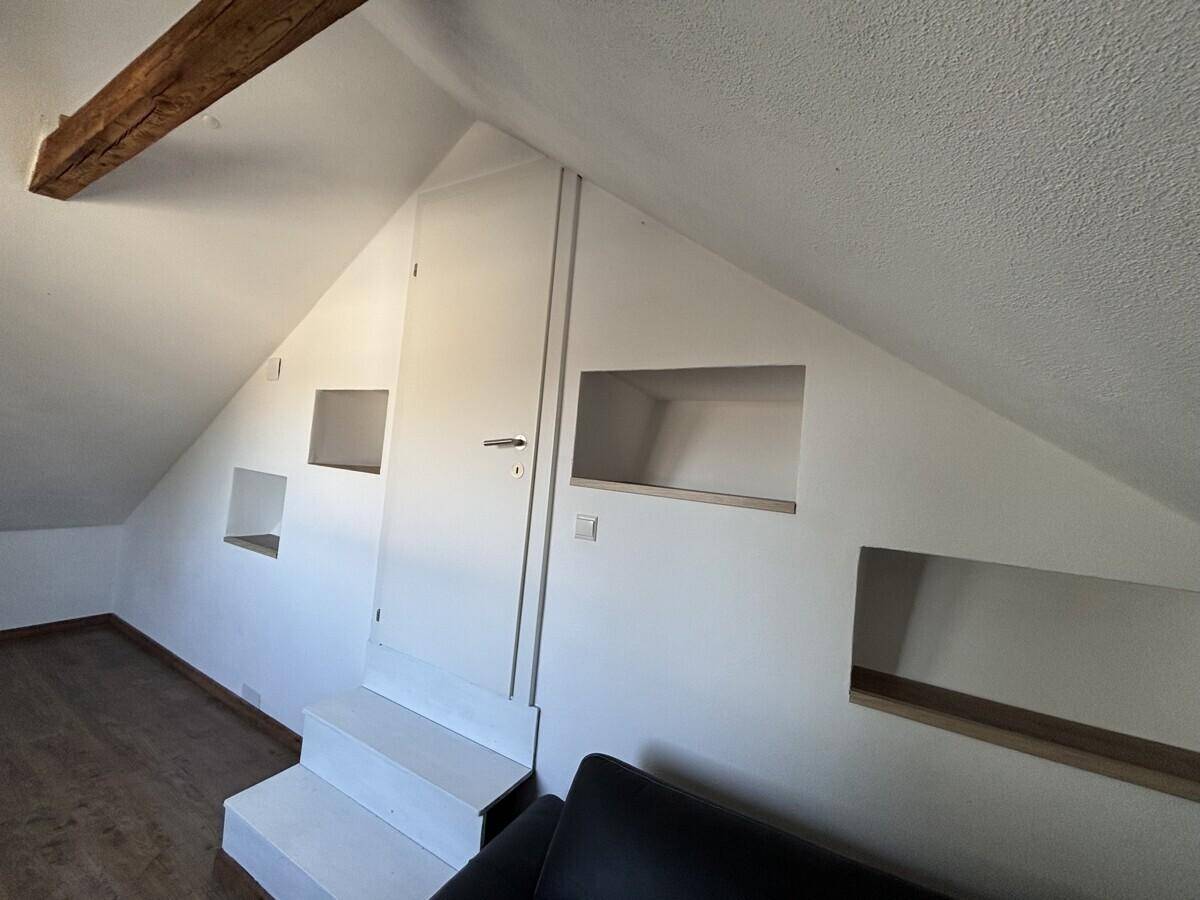 Dachbodenraum mit schrägen Wänden, integrierten Nischen und einer Tür.
