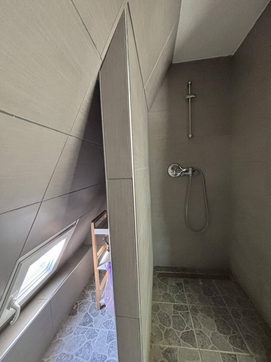 Modern gefliestes Badezimmer im Dachgeschoss mit Dusche und schräger Decke.