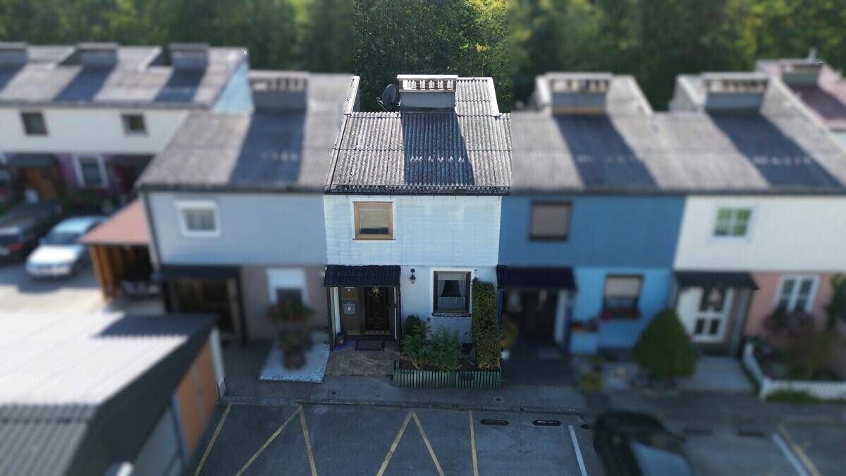 Luftaufnahme der Vorderseite eines Reihenhauses mit Parkplätzen und angrenzenden Gebäuden in einer Wohnsiedlung.