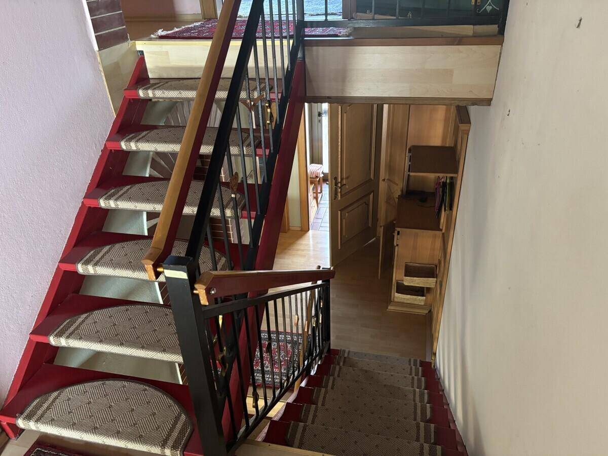 Treppenhaus, von oben fotografiert, mit rotem Teppich und Holzgeländer, das die verschiedenen Ebenen verbindet.