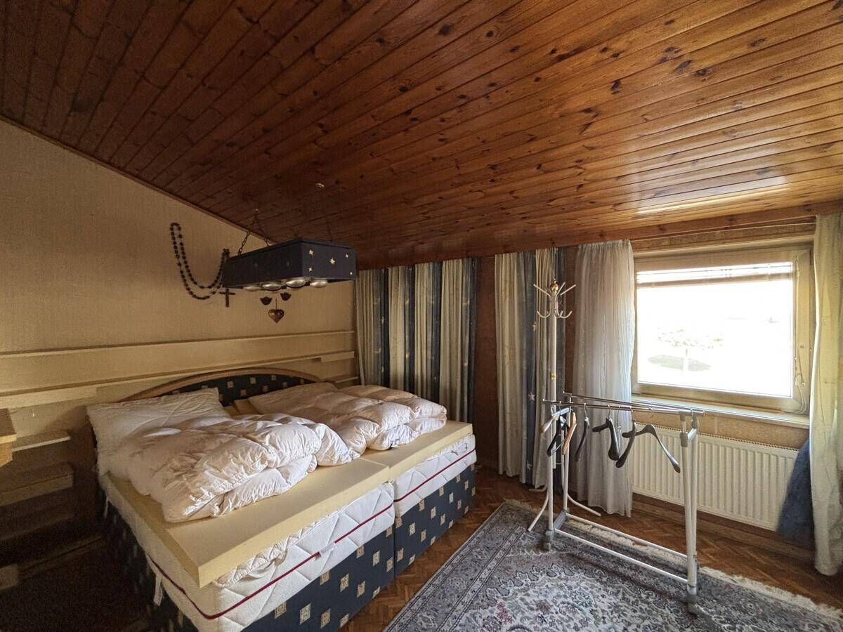 Schlafzimmer mit Doppelbett, Holzdecke und Fenster, das viel Tageslicht hereinlässt und eine gemütliche Atmosphäre schafft.
