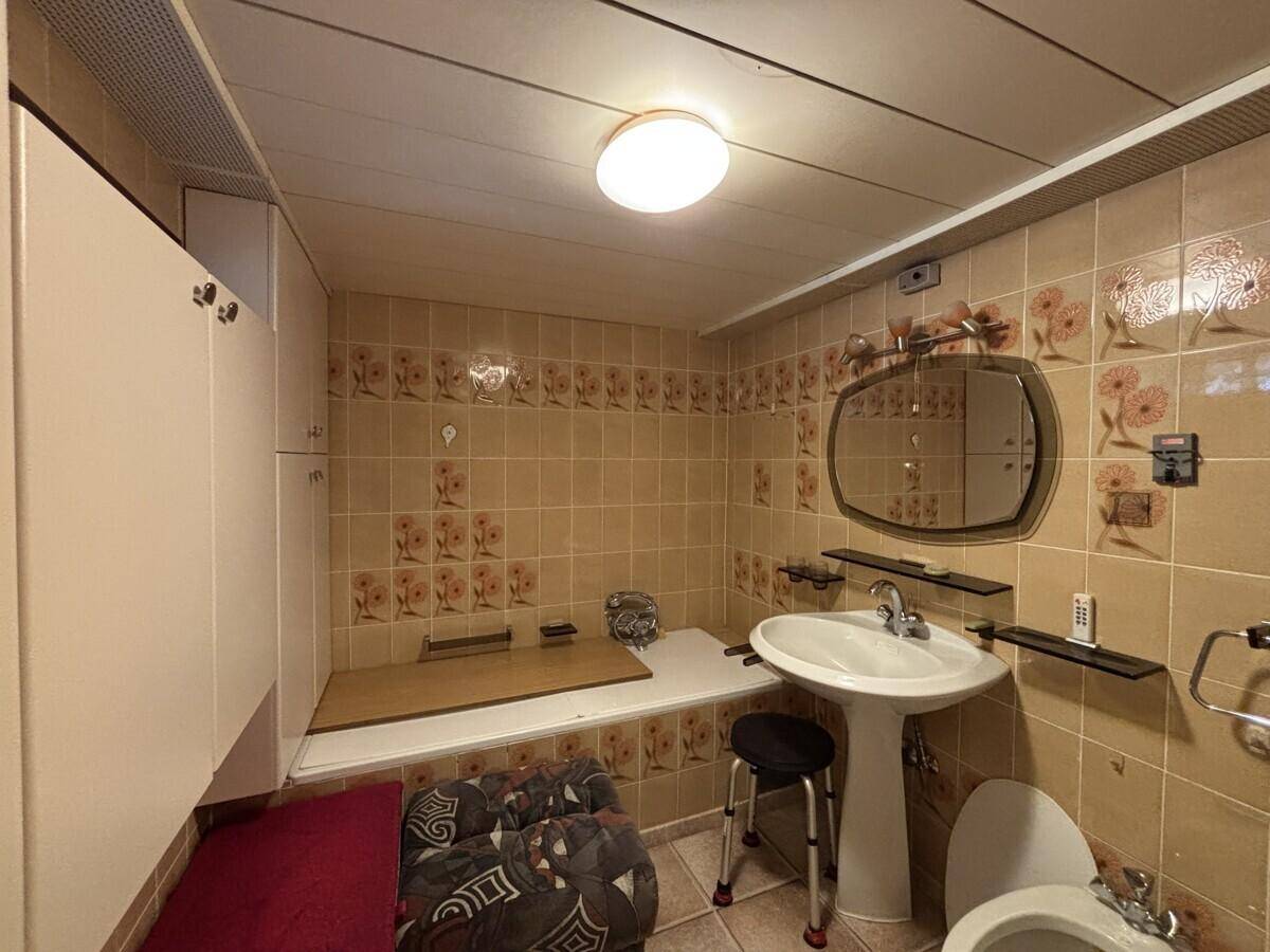 Badezimmer im Stil der 80er Jahre mit floralen Fliesen, Standwaschbecken und WC, in gutem Zustand.
