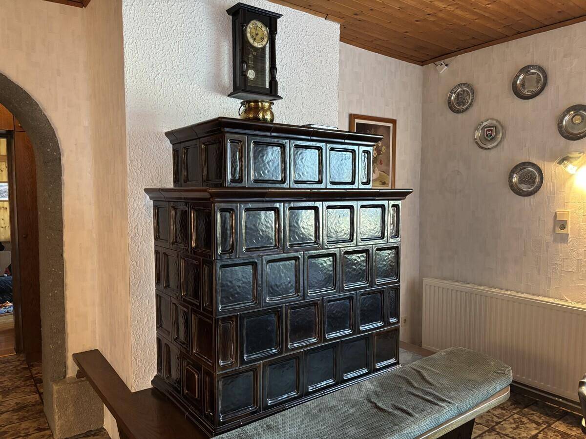 Traditioneller Kachelofen mit dunklen Fliesen und einer Sitzbank in einem gemütlichen Raum.