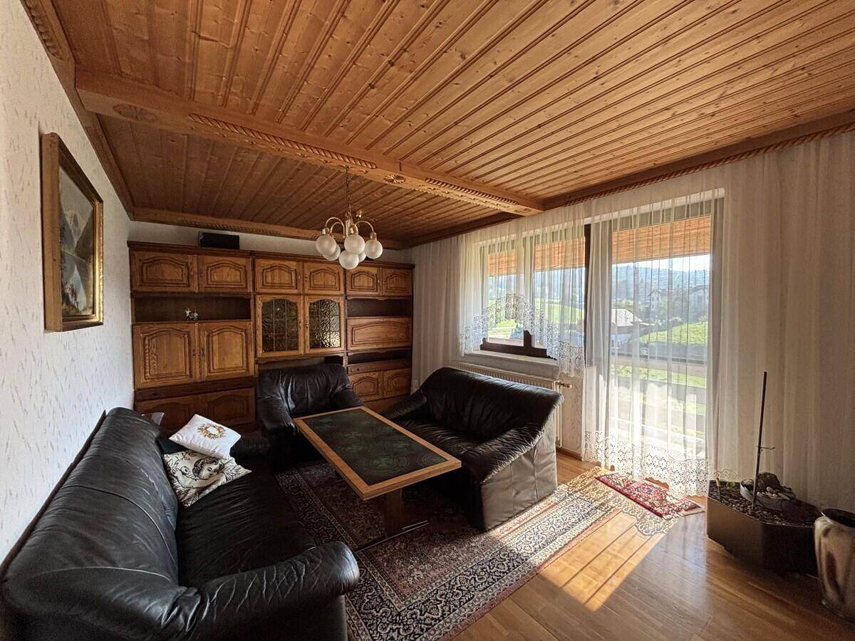 Helles Wohnzimmer mit Holzbalkendecke, Ledersofas und Zugang zu einem Balkon.