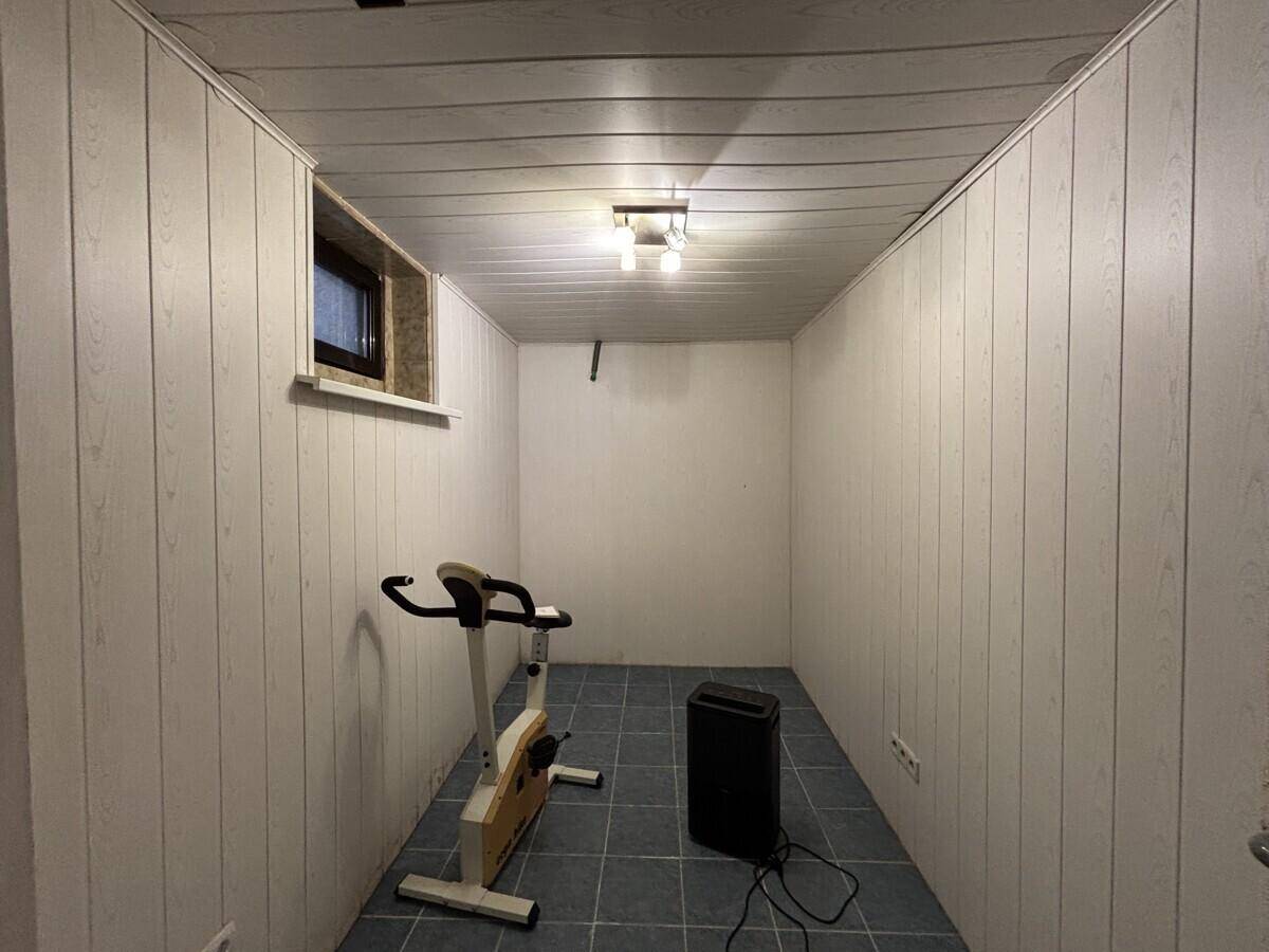 Kleiner Fitnessraum im Keller mit weißer Holzverkleidung, blauen Fliesen und einem Heimtrainer.