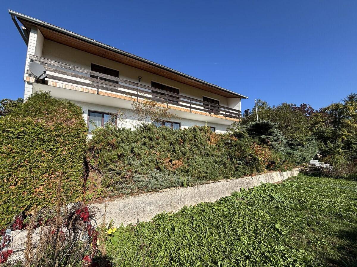 Vorderansicht des Hauses mit Balkonen und üppiger Bepflanzung im terrassierten Vorgarten.