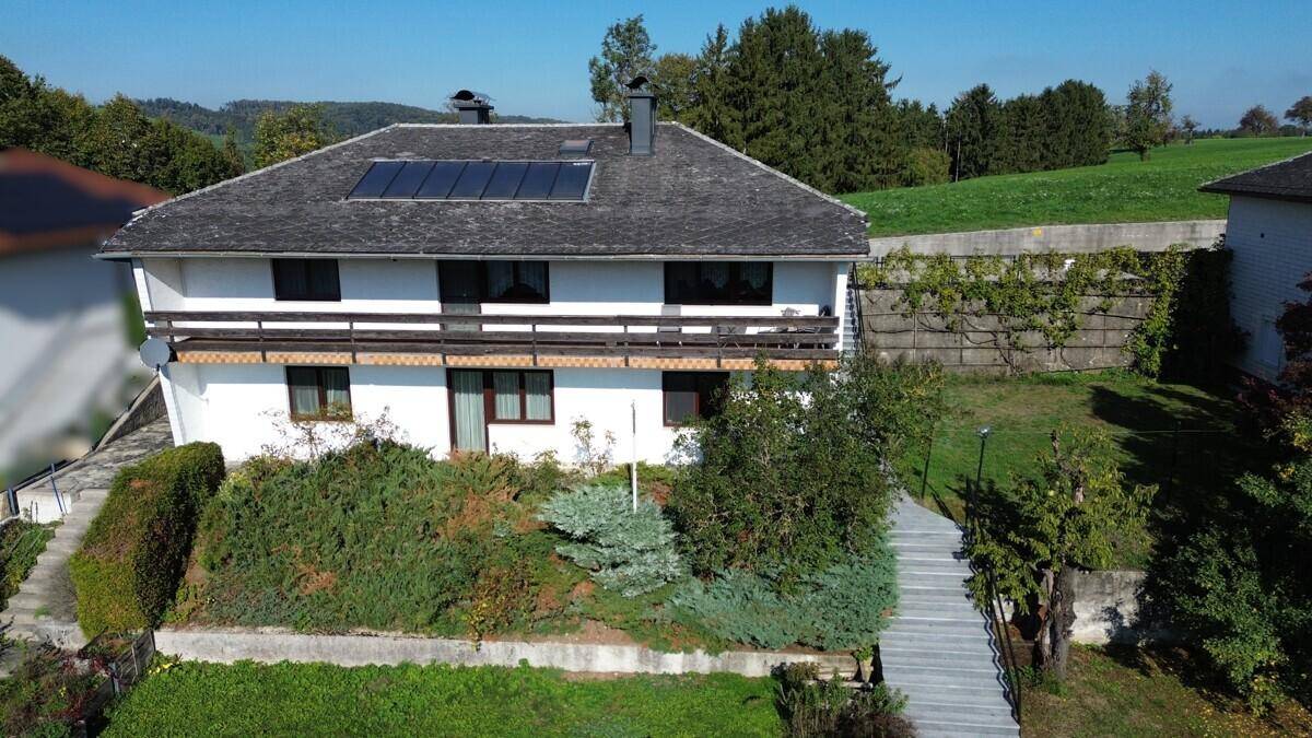 Das weiße Haus mit Photovoltaikanlage auf dem Dach und terrassiertem Garten in ländlicher Umgebung.