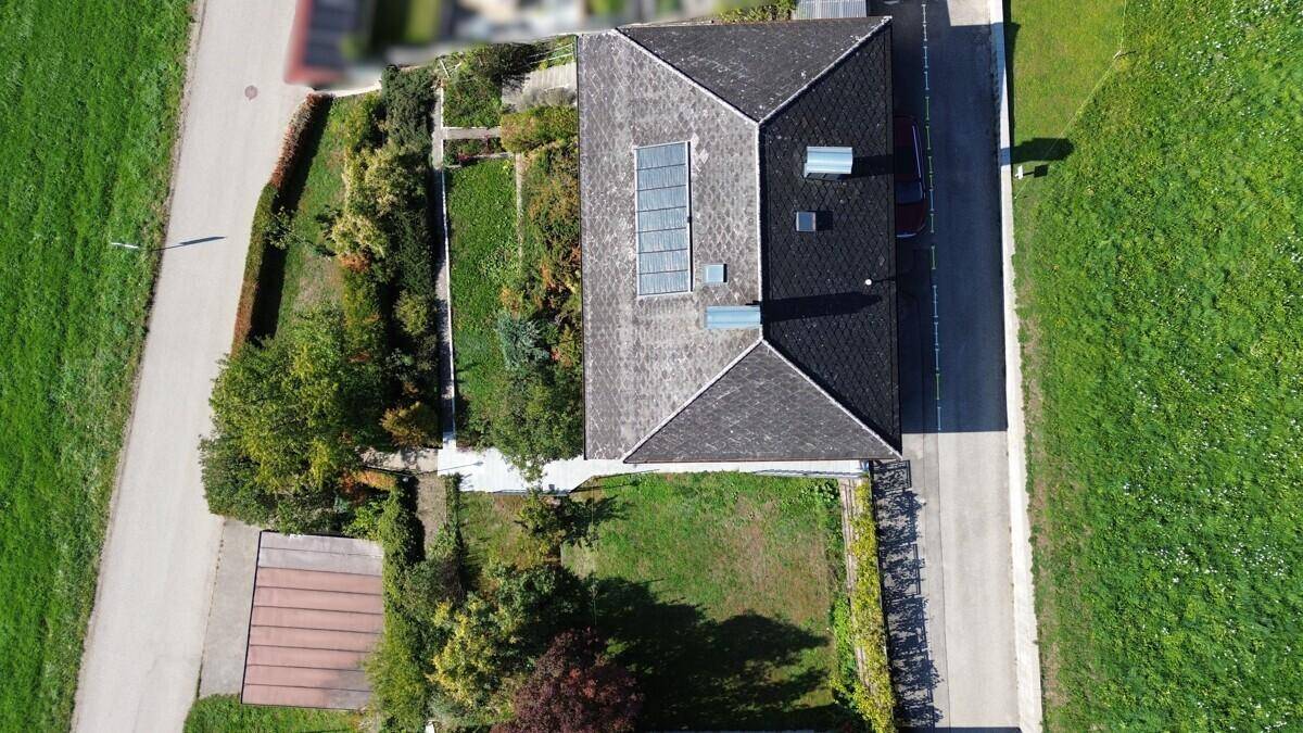 Luftaufnahme des Grundstücks mit Haus, Garten und angrenzenden Feldern unter blauem Himmel.