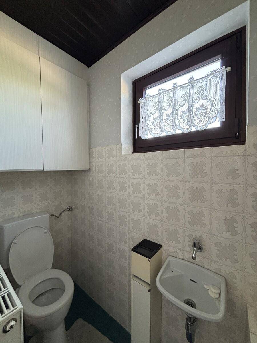 Separate Toilette mit kleinem Waschbecken und Fenster, gefliest im hellen Retro-Stil.