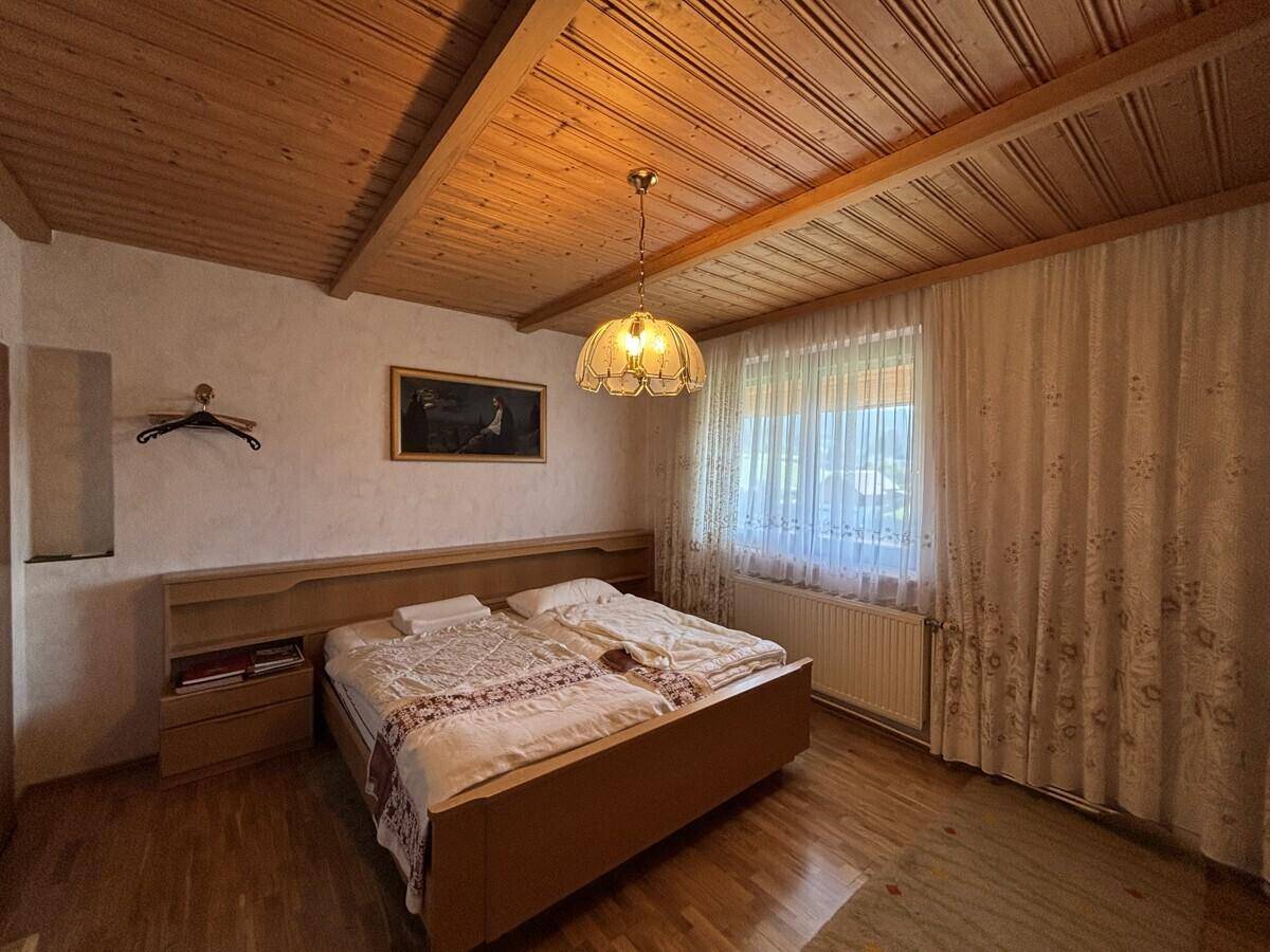 Schlafzimmer mit Holzbalkendecke, Doppelbett und Fenster mit Blick ins Grüne.