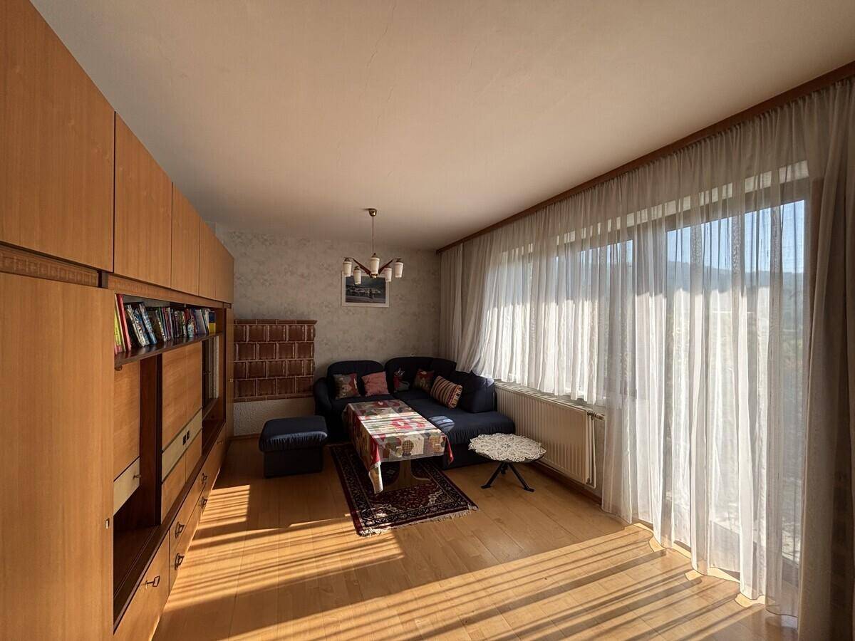 Gemütliches Wohnzimmer mit Holzboden, großem Schrank und Sofa, durchflutet von Sonnenlicht.