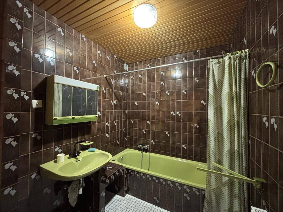 Badezimmer im Retro-Stil mit braunen Fliesen, Badewanne und grünem Waschbecken.