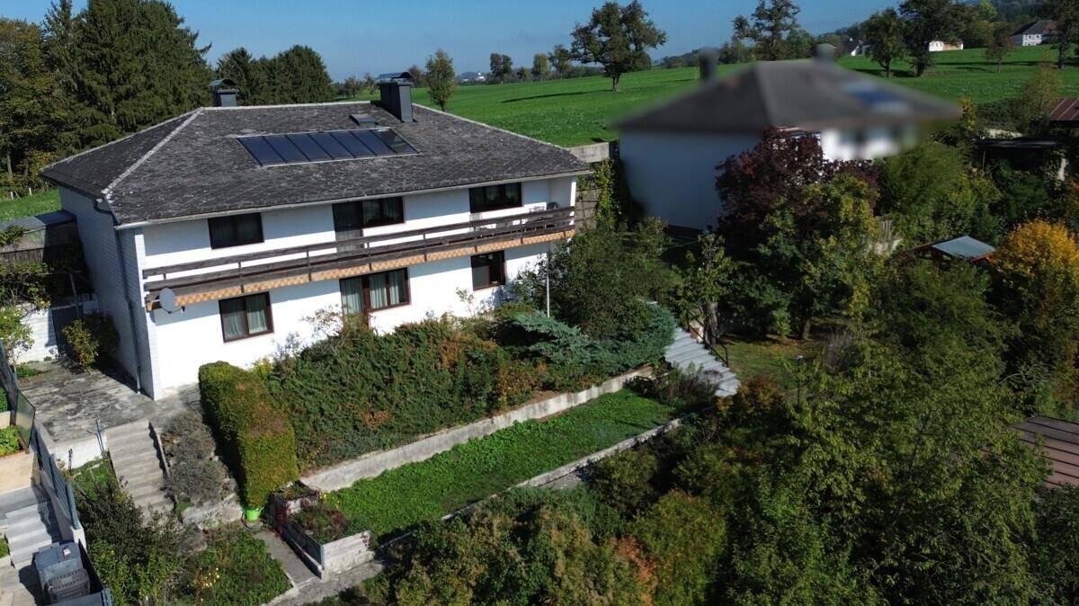 Ansicht des Hauses von oben mit Photovoltaikanlage auf dem Dach und weitläufigen Grünflächen.