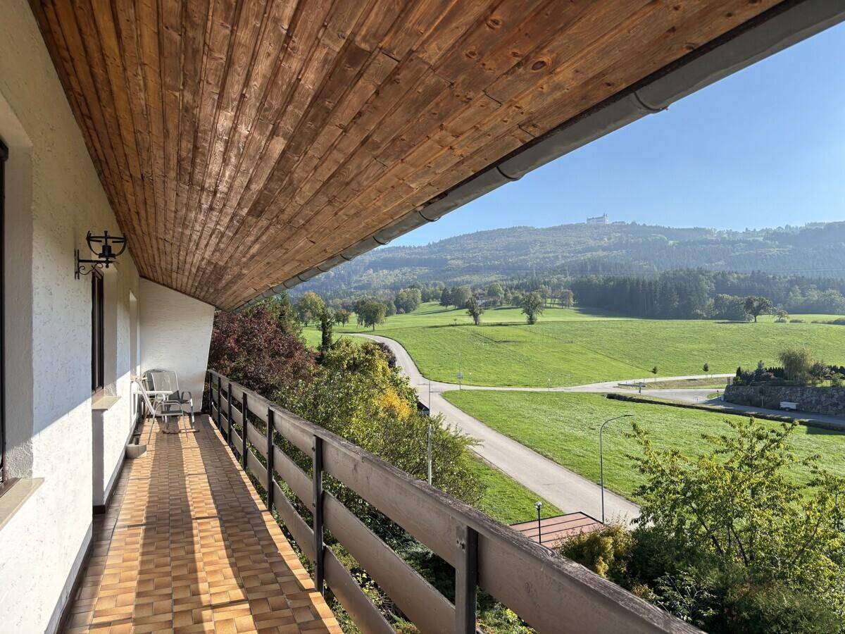 Langer Balkon mit Holzboden und weitem Blick über die grüne Hügellandschaft.
