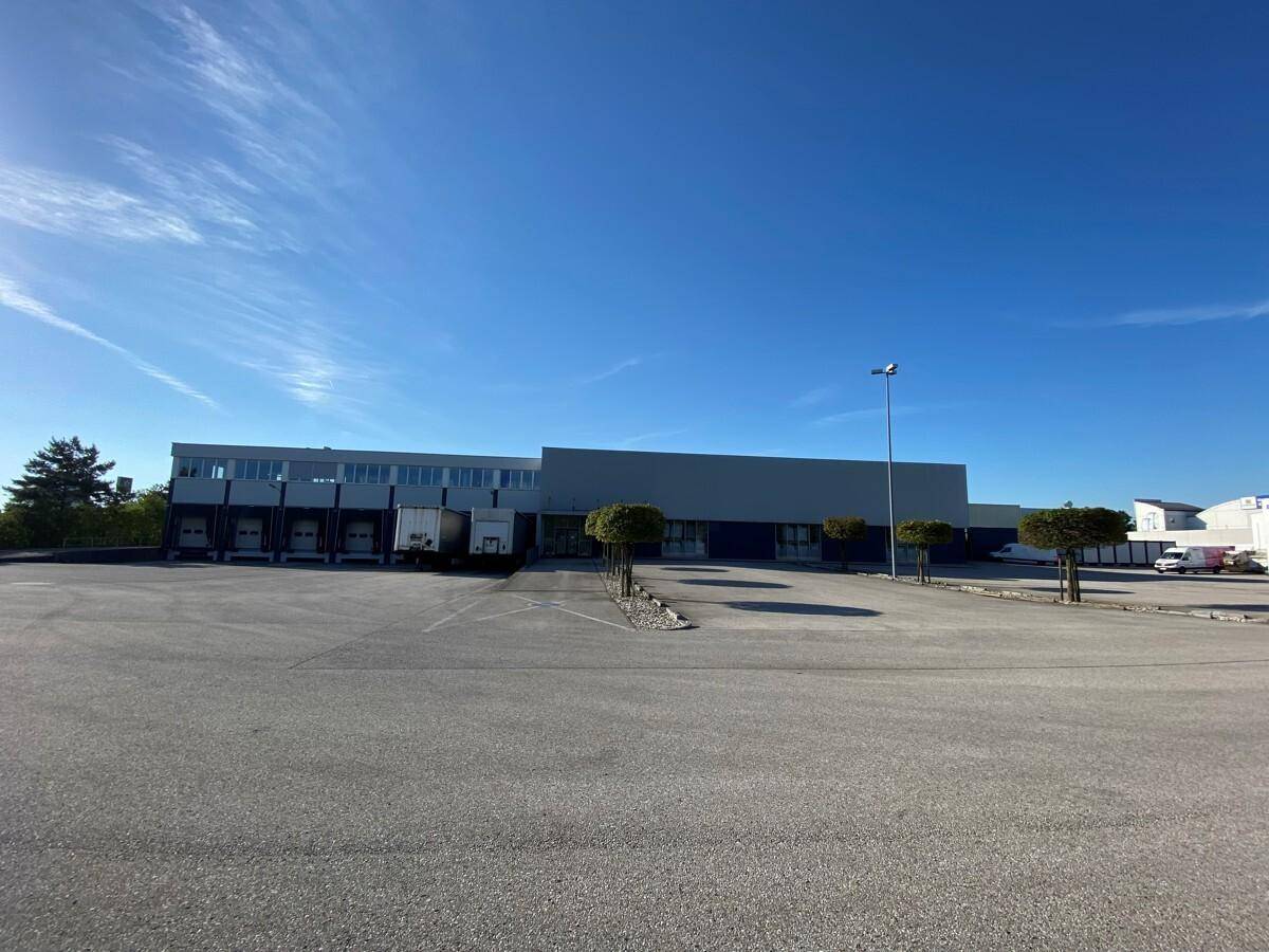 Großes Gewerbegebäude mit Laderampen und weitläufigem Parkplatz unter blauem Himmel.