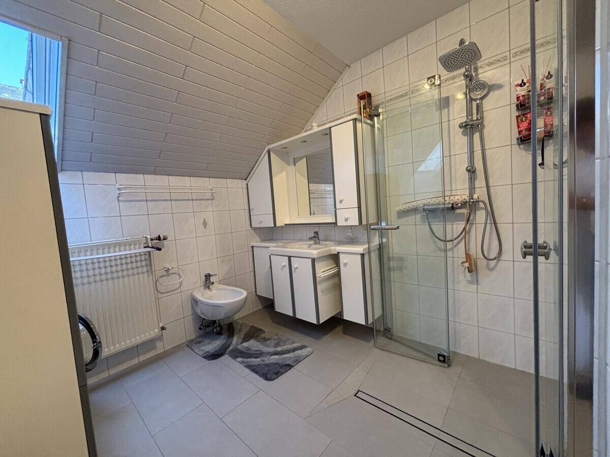 Gefliestes Badezimmer mit Dachschräge, Duschkabine, Bidet und Doppelwaschbecken.