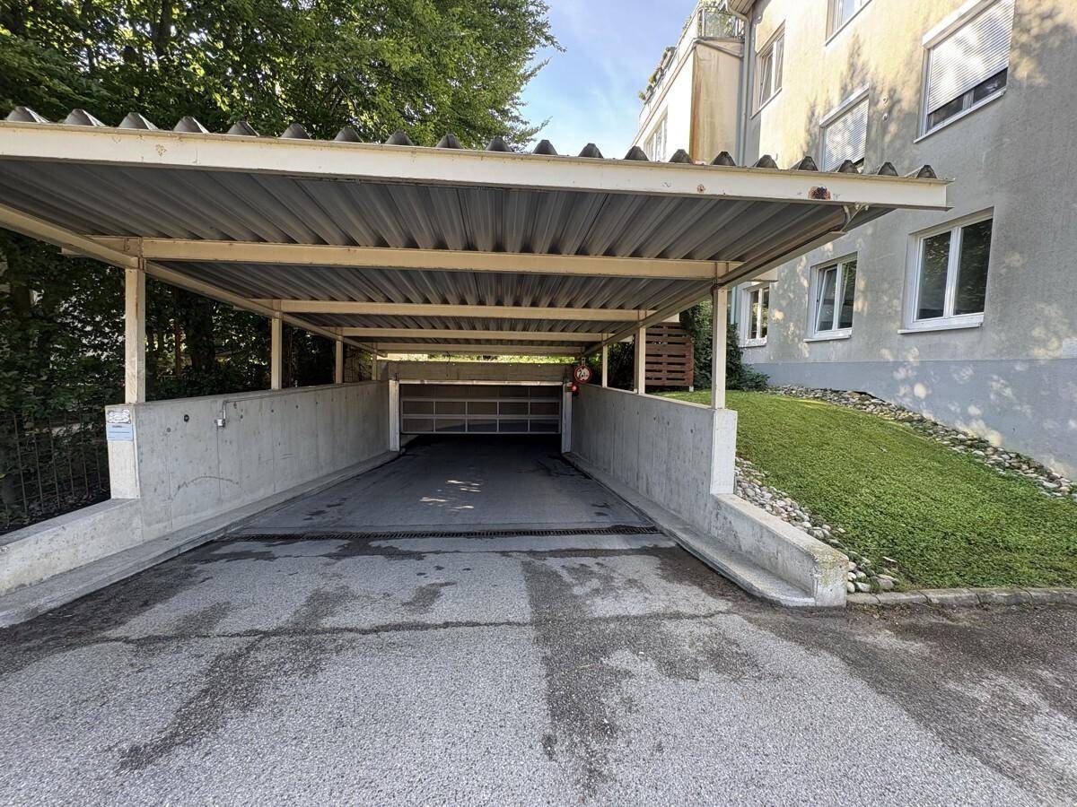 Überdachter Carport-Eingang zur Tiefgarage eines Mehrfamilienhauses mit Grünfläche.