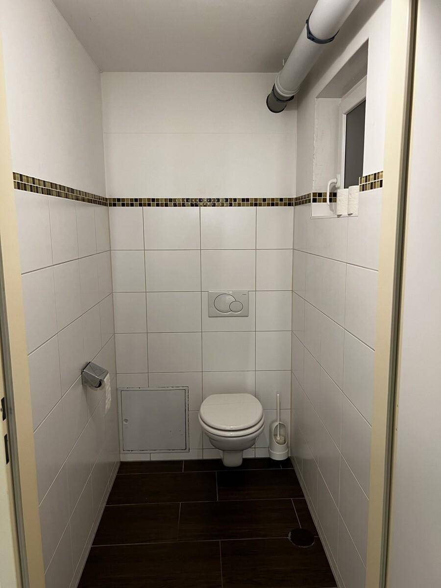 Kleiner Toilettenraum mit weißen Fliesen, wandhängendem WC und einem kleinen Fenster für Belüftung.