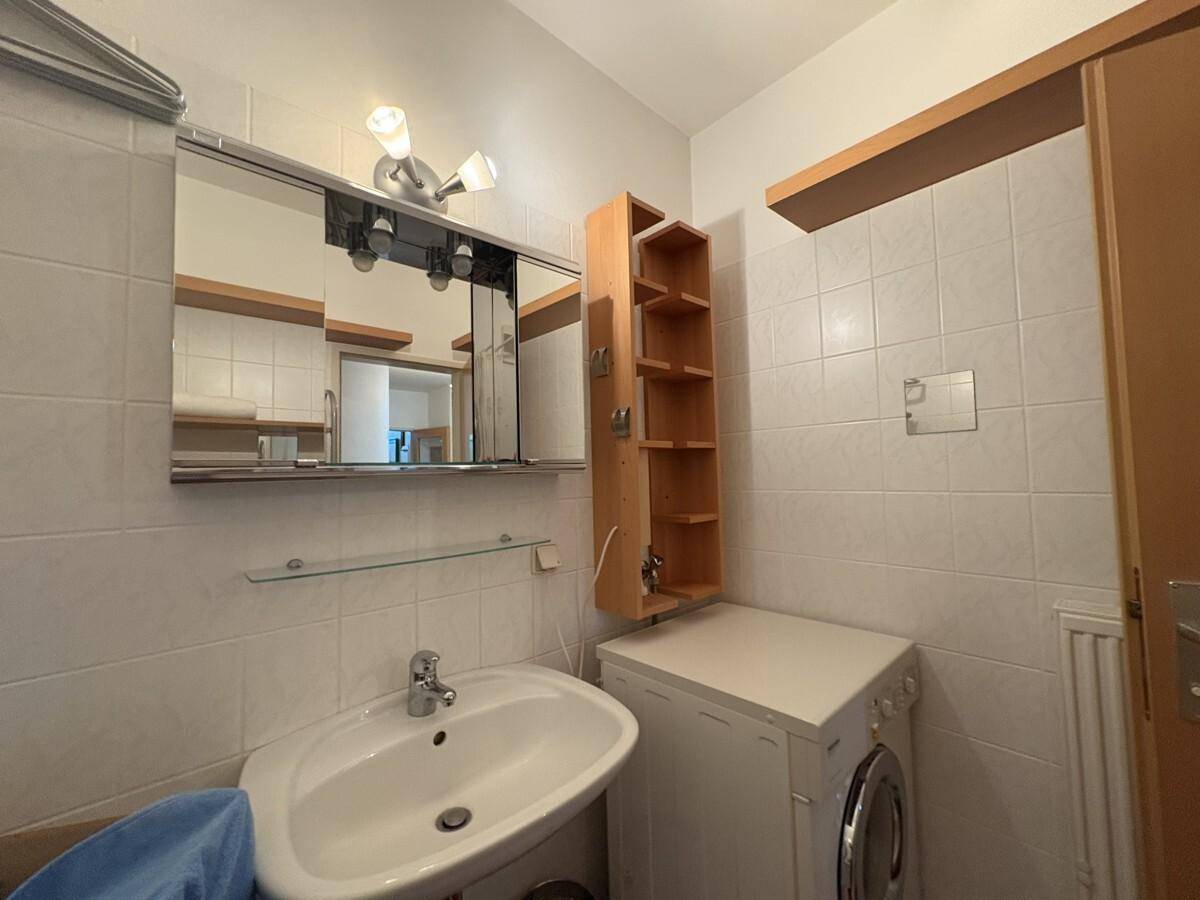 Badezimmer mit weißen Fliesen, Waschbecken und Waschmaschine, praktisch eingerichtet.