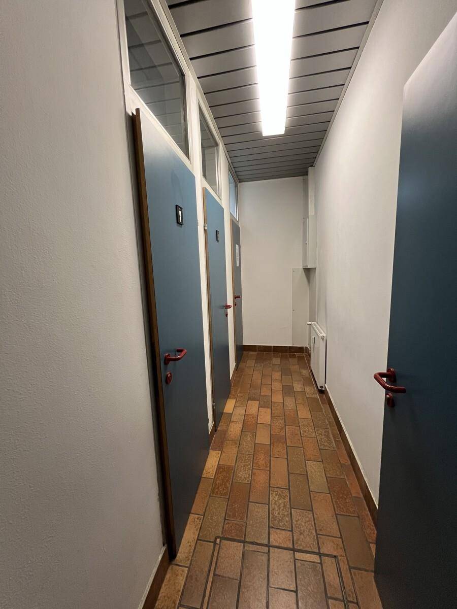 Langer Flur mit Terrakotta-Fliesenboden und mehreren Türen, gut beleuchtet.