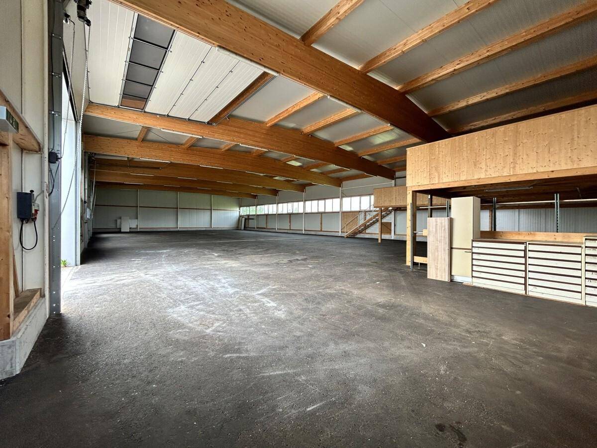 Helle und offene Industriehalle mit Holzbalkenkonstruktion, Oberlichtern und einem erhöhten Lagerbereich im Hintergrund.