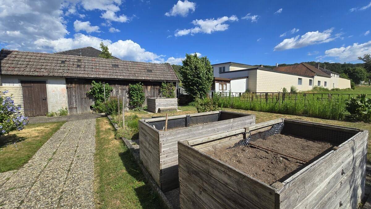 Gartenbereich mit Hochbeeten, einem rustikalen Schuppen und viel Grünfläche.