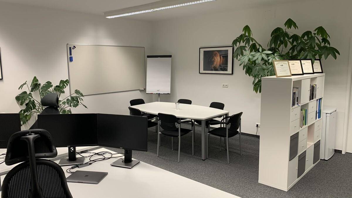 Heller Büroraum mit Konferenztisch, Whiteboard und Regalsystem für Akten und Dekoration.
