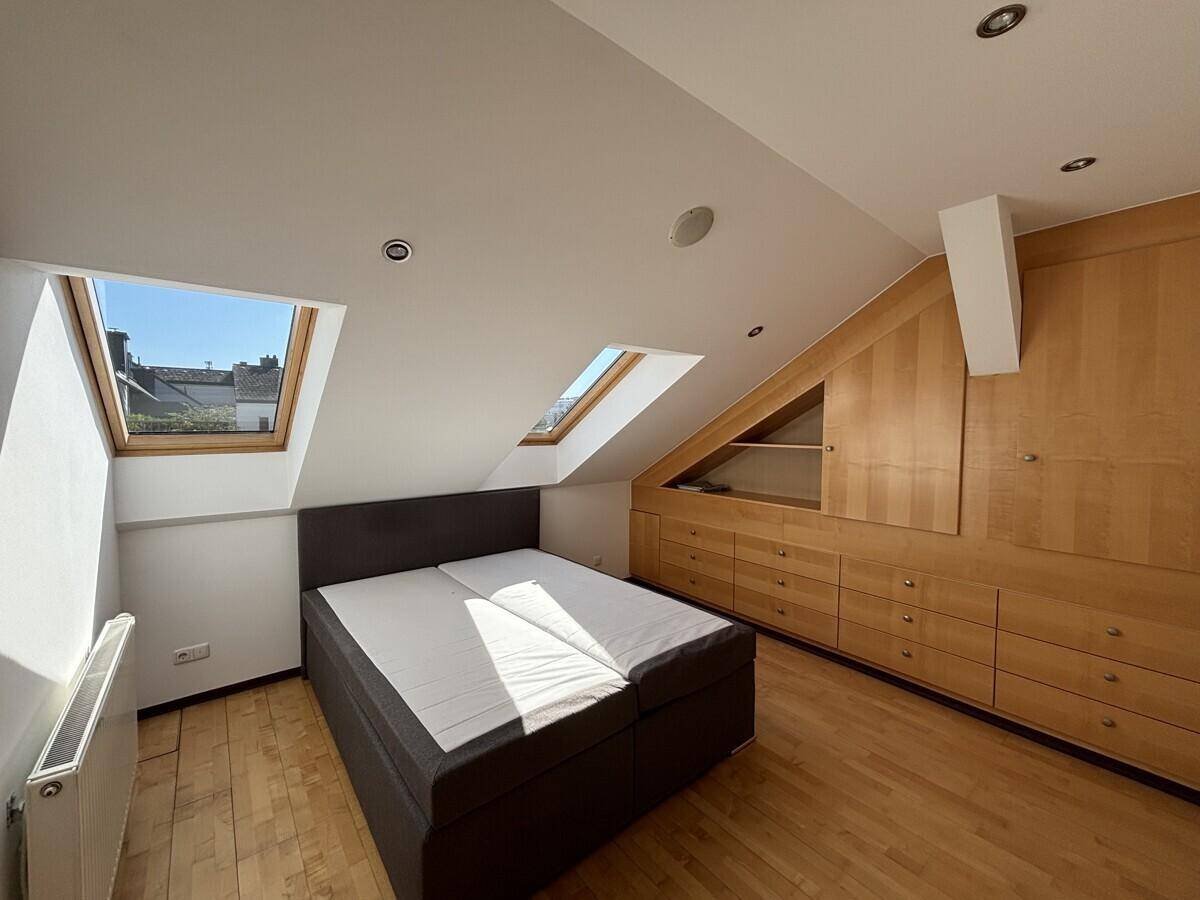 Schlafzimmer im Dachgeschoss mit Doppelbett, Einbauschränken und viel Tageslicht durch Dachfenster.