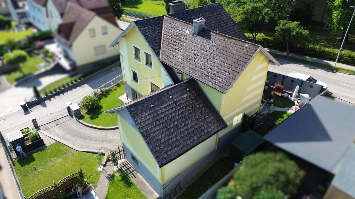 Schrägansicht eines Einfamilienhauses mit gelber Fassade und Satteldach in ländlicher Umgebung.