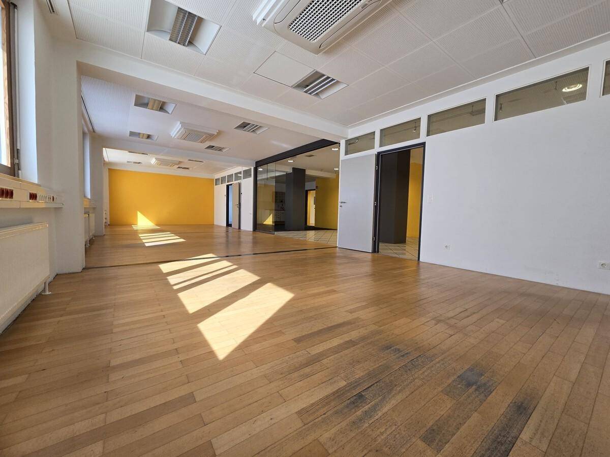 Heller Büroraum mit Holzboden, gelber Akzentwand und einer großen Spiegelfläche, die den Raum erweitert.