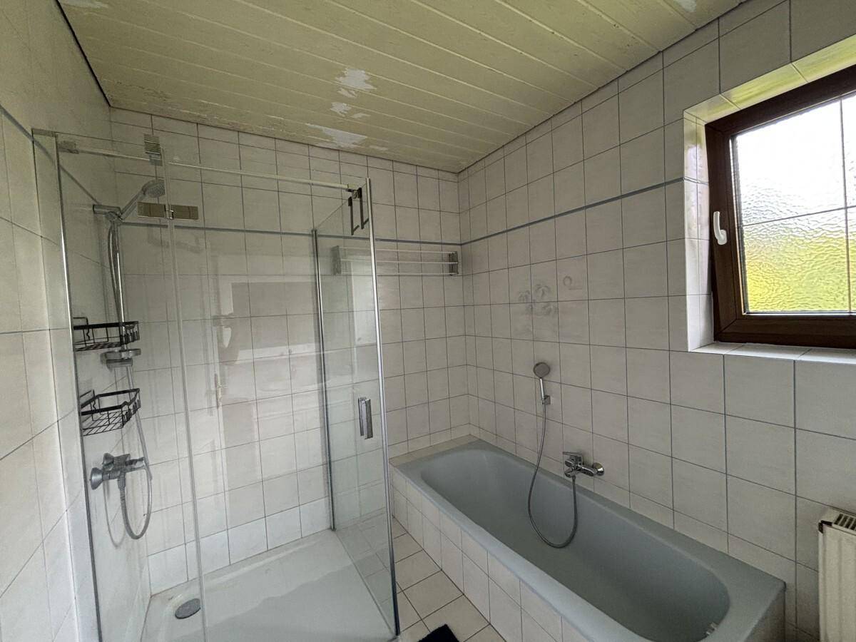 Badezimmer mit Badewanne, Duschkabine und Fenster für natürliches Licht.
