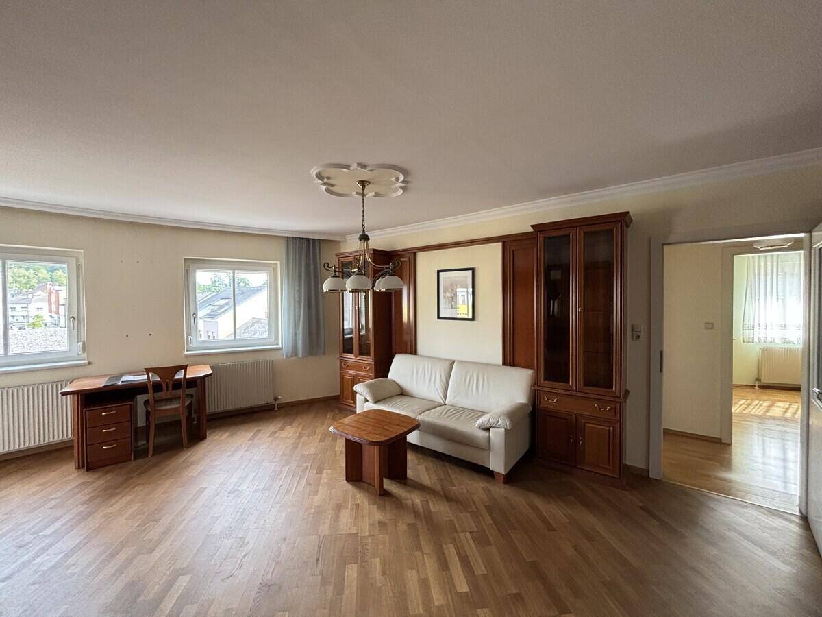 Helles Wohnzimmer mit Parkettboden, Schreibtisch und Blick ins Grüne.