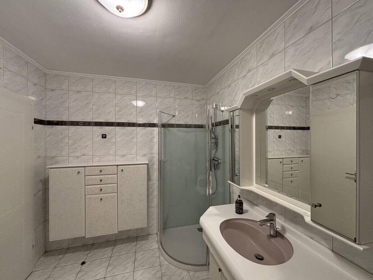 Badezimmer mit hellen Fliesen, Dusche und integriertem Spiegelschrank.