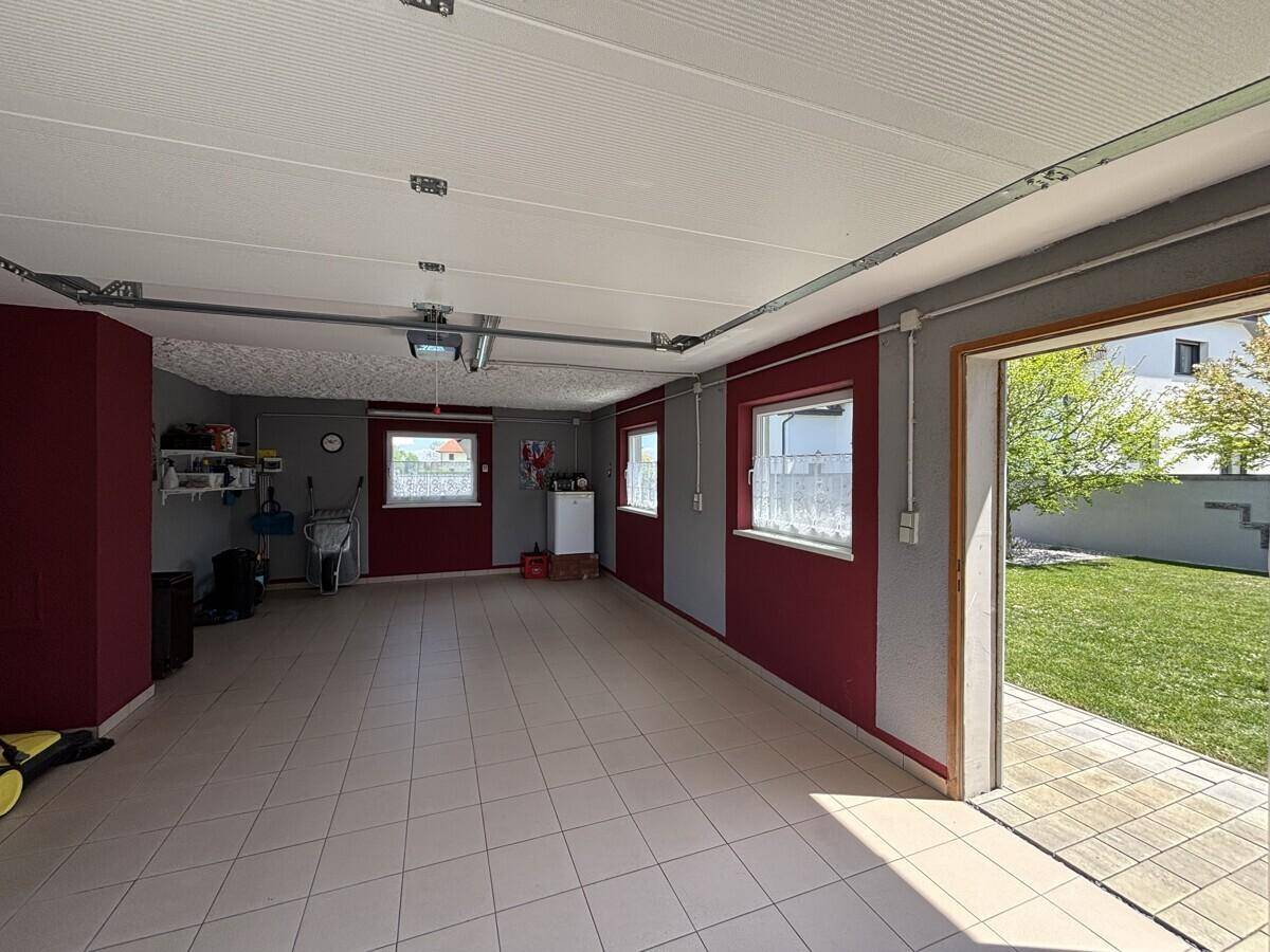 Geräumige Garage mit Fliesenboden, Fenstern und direktem Zugang zum Garten.
