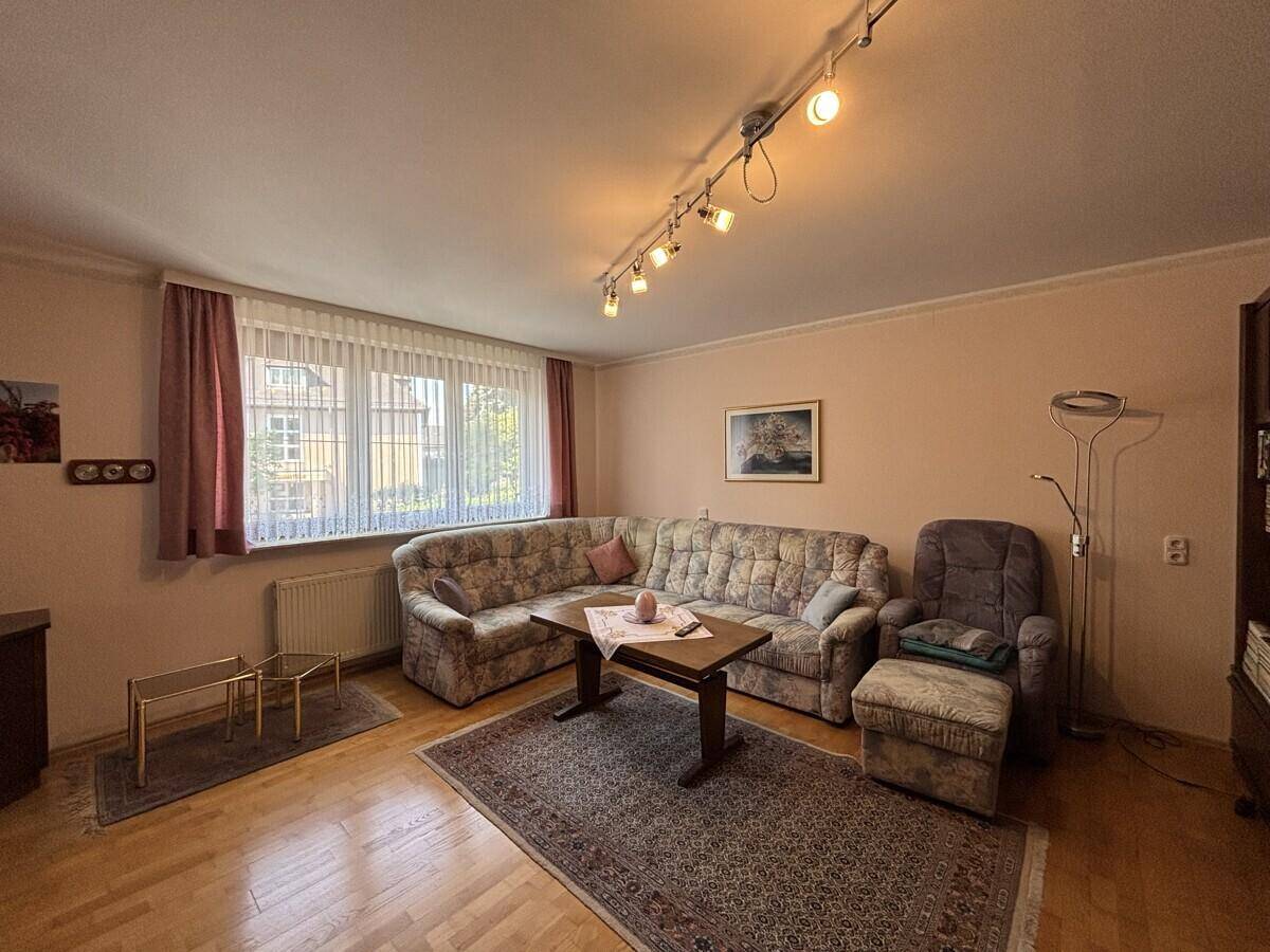 Gemütliches Wohnzimmer mit floral gemustertem Sofa, Holzboden und Blick ins Grüne.