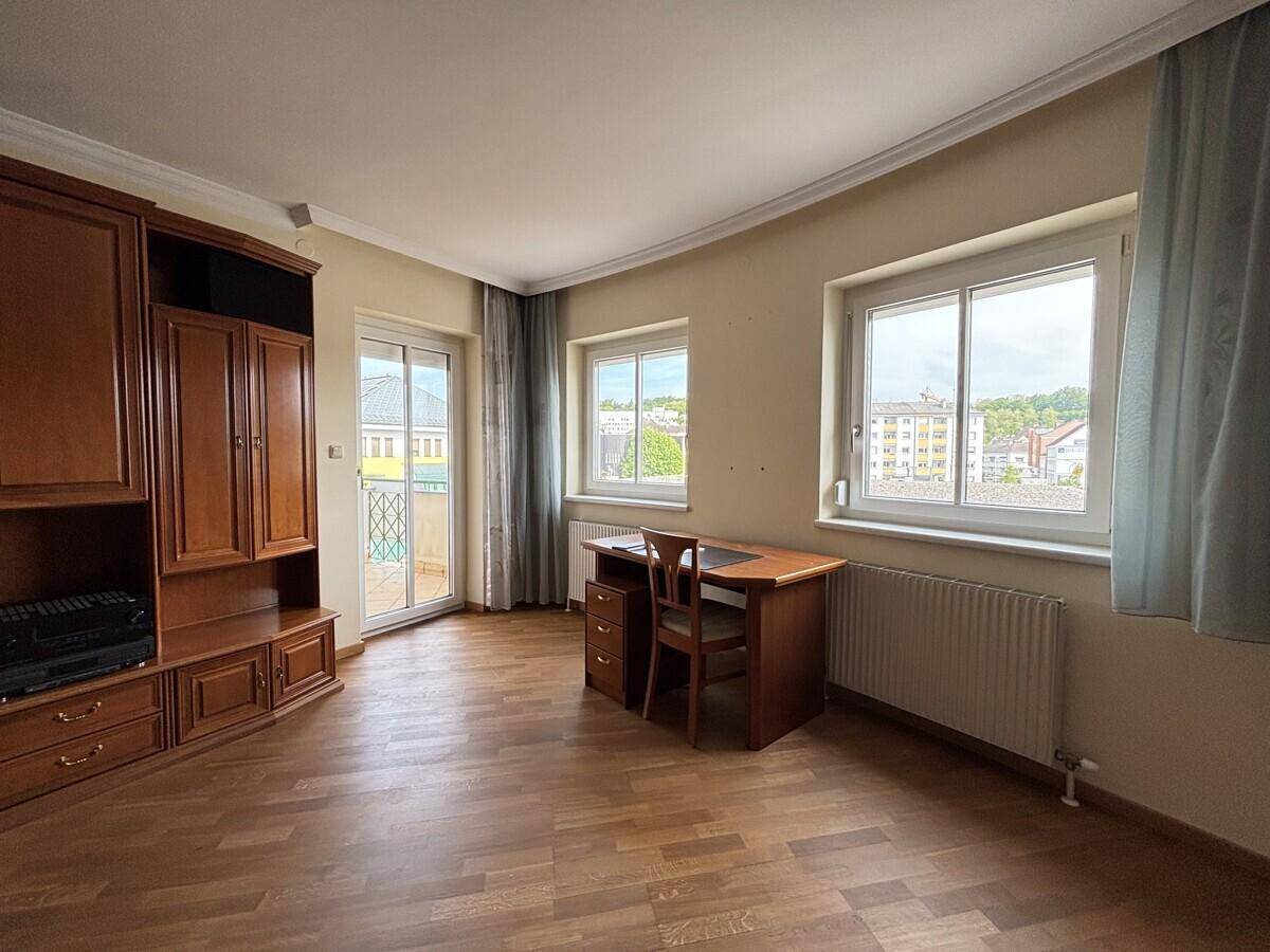 Wohnraum mit Parkettboden, Schreibtisch und Zugang zu einem Balkon.