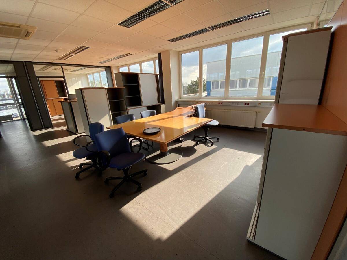 Heller Büroraum mit großem Holztisch, Bürostühlen und Schränken, durchflutet von natürlichem Licht.
