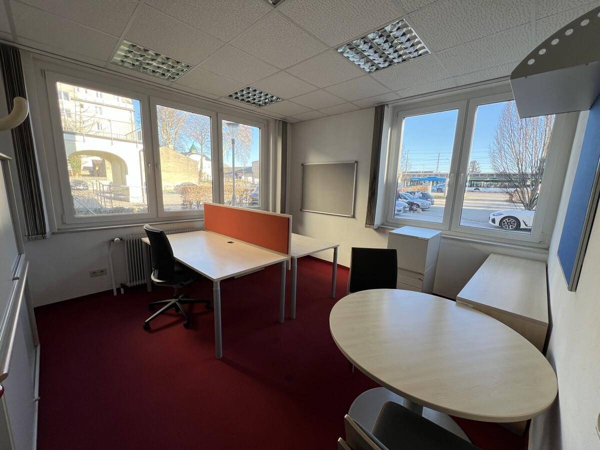Helles Büro mit rotem Teppichboden, mehreren Arbeitsplätzen und großen Fenstern.