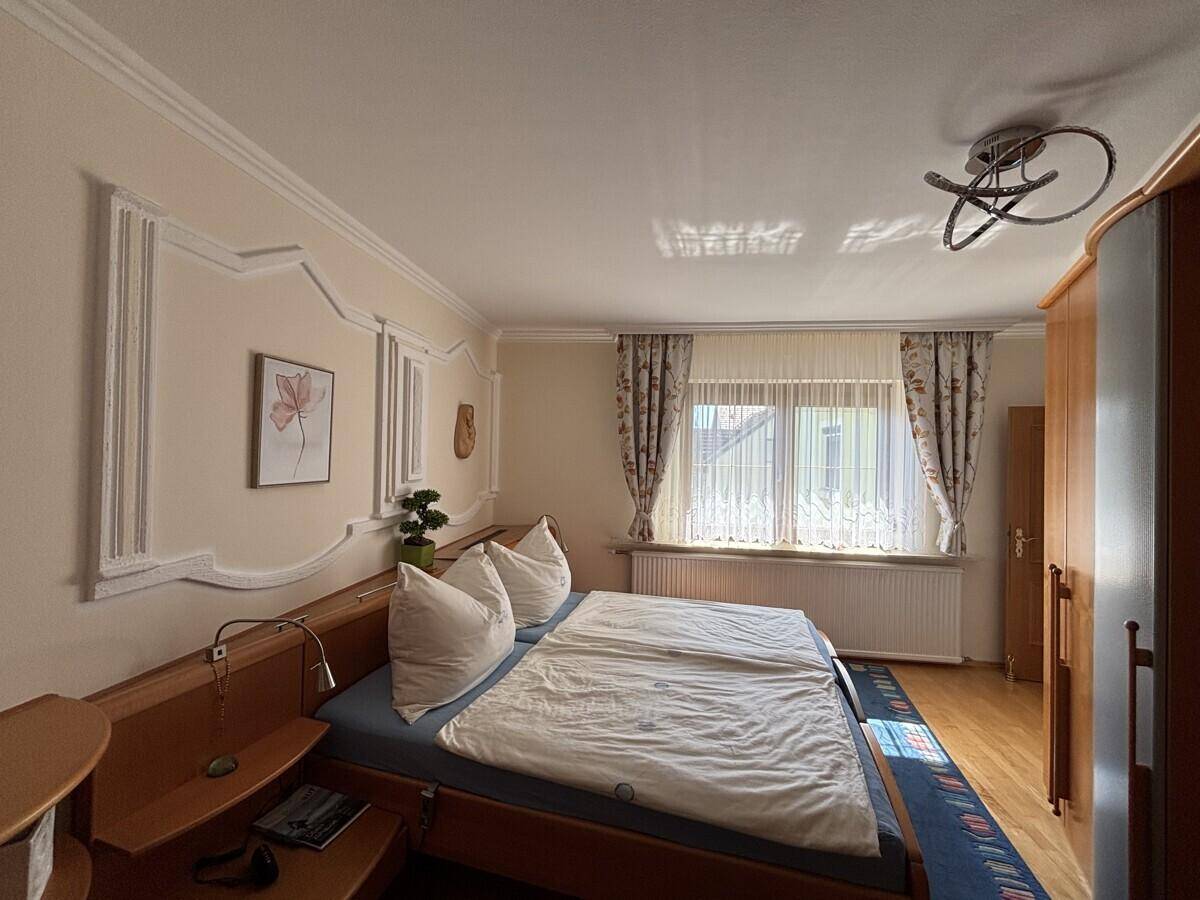 Helles Schlafzimmer mit Doppelbett, Holzmöbeln und Fenster mit Vorhängen.