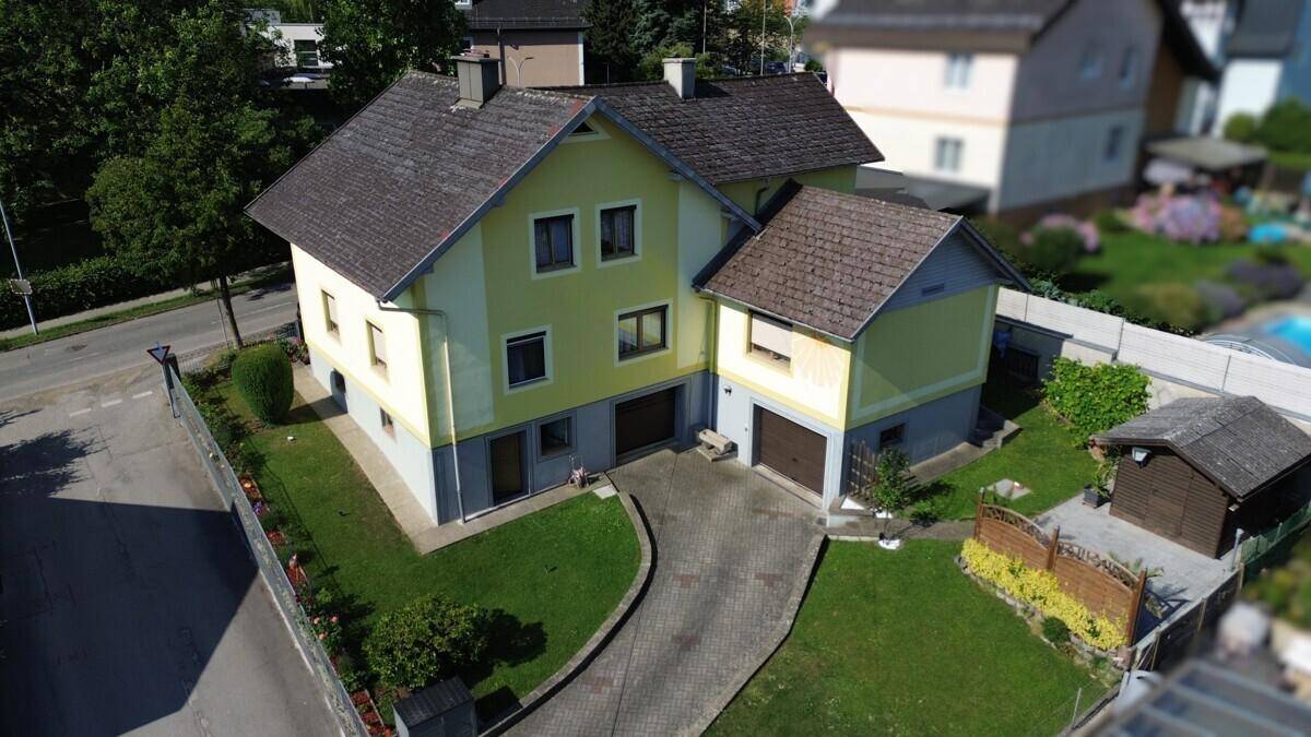 Ansicht eines Einfamilienhauses mit gelber Fassade, Garage und gepflegtem Vorgarten.