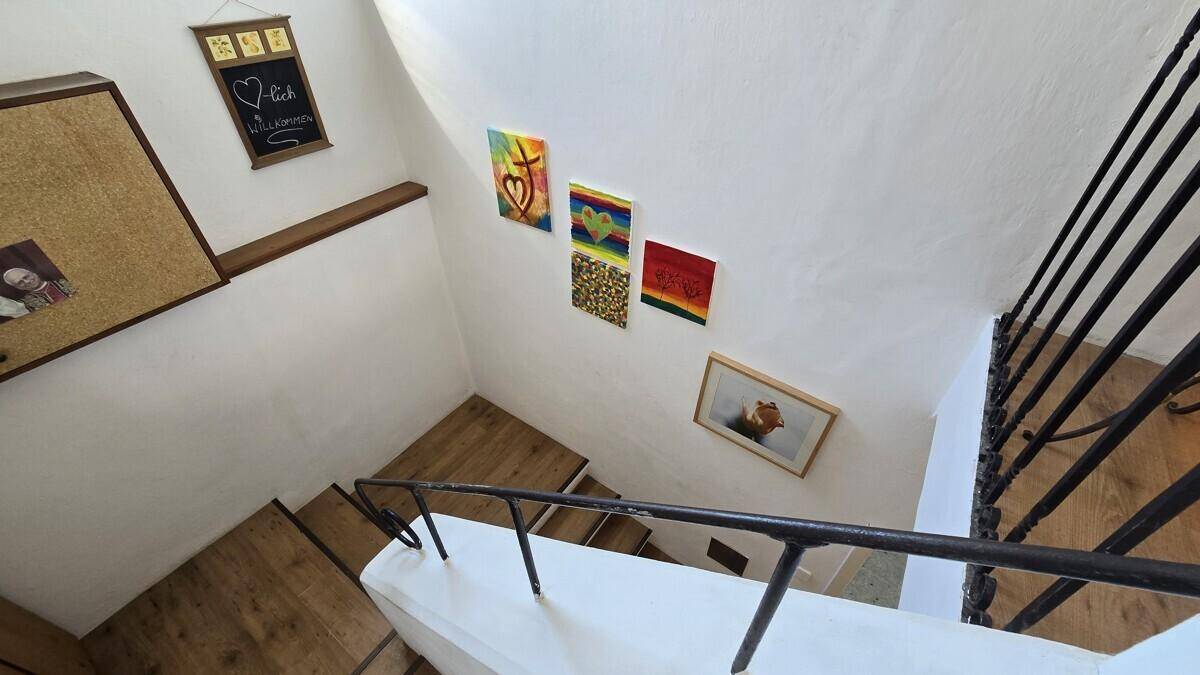 Helles Treppenhaus mit Holzstufen, schmiedeeisernem Geländer und dekorativen Bildern an der Wand.
