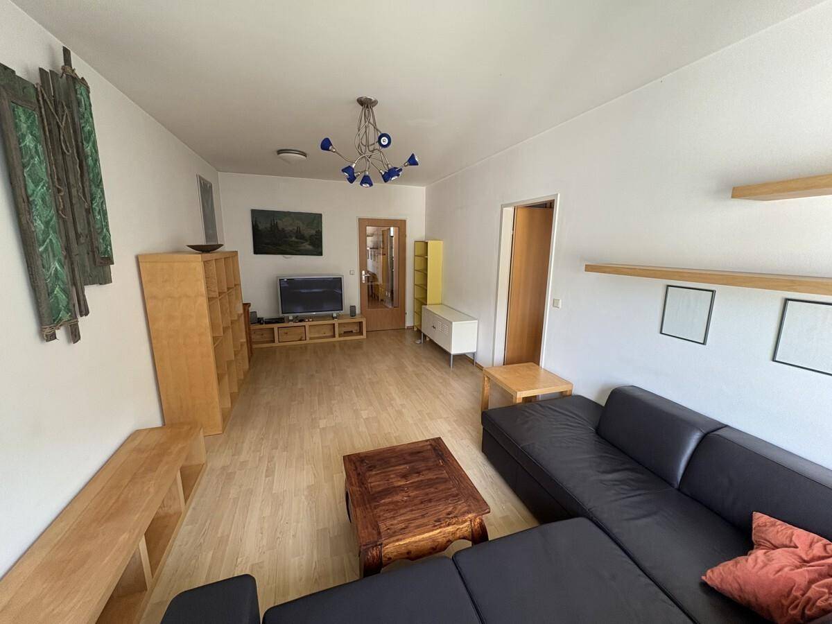 Gemütliches Wohnzimmer mit schwarzem Sofa, Holzmöbeln und Laminatboden, einladend eingerichtet.
