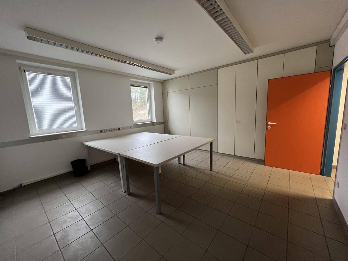 Helles Büro mit zwei Fenstern, Fliesenboden und einer auffälligen orangefarbenen Tür.